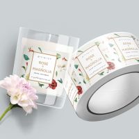 Circle-shaped image of custom printed labels on roll and adhered to candle next to flower