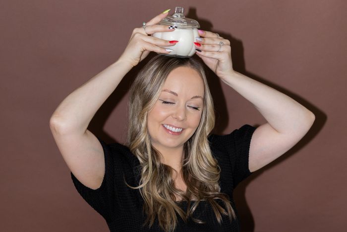 Mad Candle Co. founder Maddie Martin playfully holding a pumpkin-scented candle on her head, smiling.