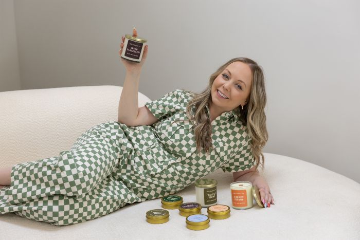 Mad Candle Co. founder Maddie Martin lying on a bed, smiling and surrounded by dozens of her handmade candles.