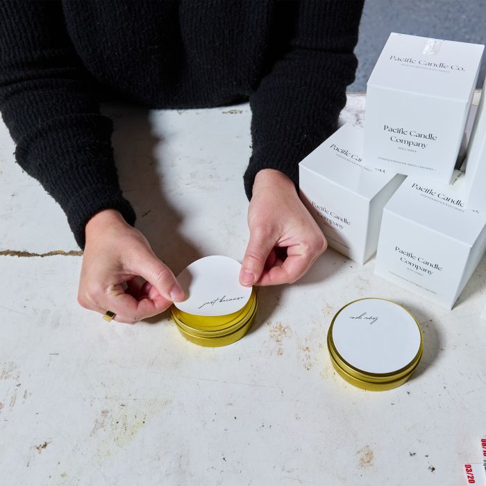 pacific candle co owner adding Avery Round labels to her candle tins 