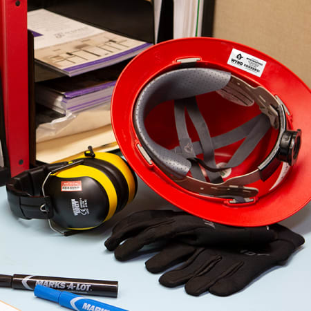 red hardhat flipped upside down showing PPE label alongside labeled earmuffs, labeled industrial gloves, and Avery Marks-A-Lot Permanent Markers