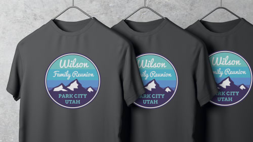 Three black t-shirts with a colorful circular design applied to each. The design is a vector illustration of purple mountains capped with snow, with a cool-toned sky behind it and text reading, 'Wilson Family Reunion, Park City, Utah'