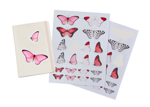 Flatlay of Avery DIY Glitter Stickers with printed pink butterfly designs next to a plain notebook with glitter butterfly stickers on the cover.