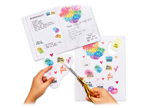 Flatlay image of person cutting up sheets of DIY sticker paper to make their own unique planner stickers