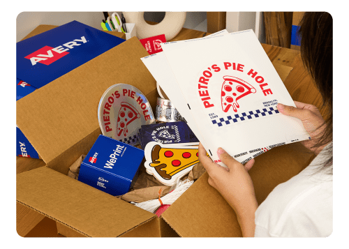 A person opening a box of small business-branded Avery labels, stickers, and cards.