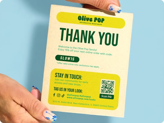 A tall promotional packaging insert card with a bright green and yellow design, showcasing a special discount offer for the customer's next order. It is held at the corners by two hands, and is sitting against a light blue background.