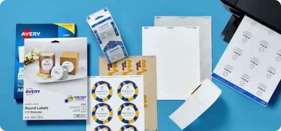 Flatlay on sky blue background of two packs of labels, four sheets of labels in varying materials, a printed roll of labels, a blank roll of labels, and a black printer on the right printing labels with a clean typography design,