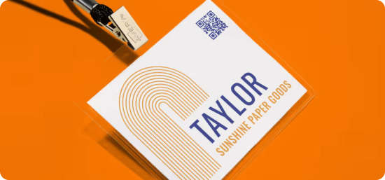 Name tag in a plastic hanging badge name holder on a black lanyard, leaned against a deep orange background.