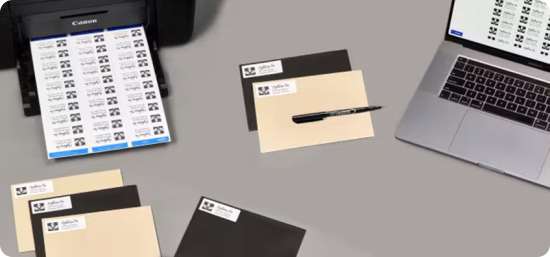 A printer printing a sheet of labels, next to a black and beige set of file folder labels and a laptop