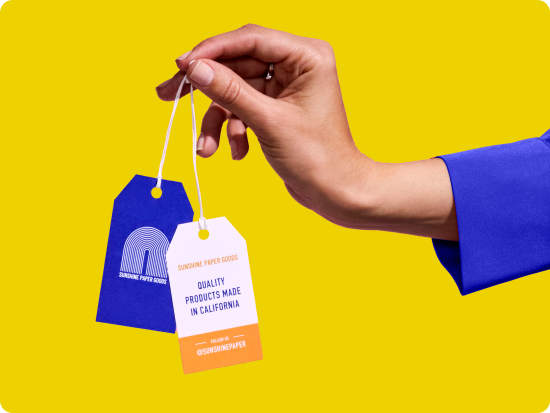 Person holding two hanging tickets with blue and orange designs, with index finger and thumb against a bright yellow background.