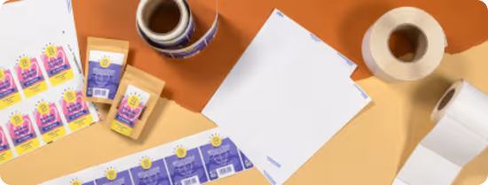 An overhead view of sheet labels and roll labels with a purple design, against a light and dark brown work surface