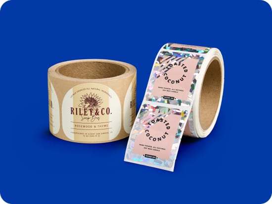 Two sheets of custom printed labels, one with a deep blue arch design and one with a bright orange round design, beind held by a hand that has burst through a large sheet of blue paper, which occupies the background