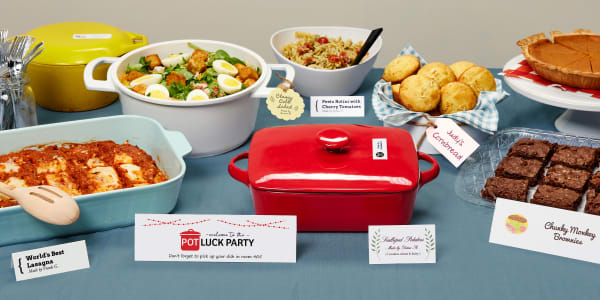 An example of a buffet table for an office potluck. Each dish on the table is labeled with a card or tag indicating information about the dish. Some of the pots are labeled to ID the owners. 