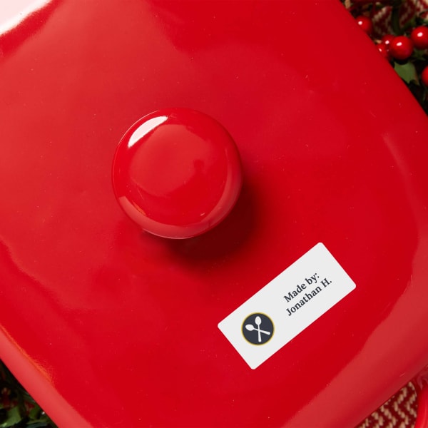 A close up of a bright red baking dish lid. Avery dissolvable label 4224 is used to ID the baking dish owner. The label features a crossed spoons design and reads, "Made by: Jonathan H."