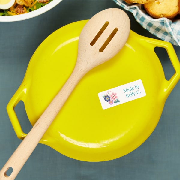 A top view of a bright yellow baking dish lid. Avery removable label 6460 is used to ID the baking dish owner. The label features a teal and pink floral design and reads, "Made by Kelly C."