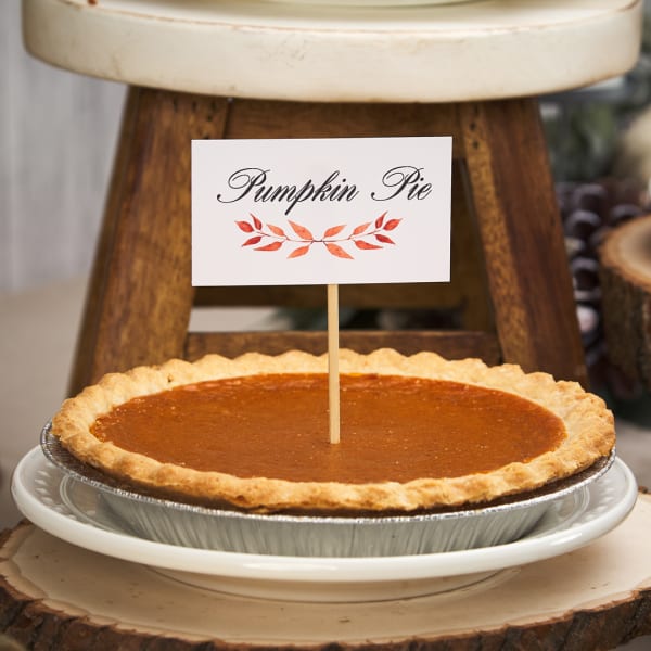 Avery place card 5302 is glued on a skewer that has been stuck in a pumpkin pie. The card reads, "Pumpkin Pie" in swirly elegant font and is accented by a simple fall foliage branch. 