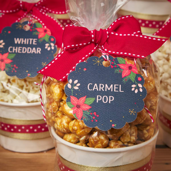 Avery tags 80511 are printed with a festive poinsettia print on a dark blue background. Cups of popcorn are labeled "white cheddar" and "caramel pop,"