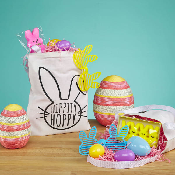 An Easter display showing off oversized Easter egg decorations and a tote bag filled with treats instead of a traditional Easter basket. The reusable tote features an Avery template for fabric transfer 3271 that reads, "Hippity Hoppy" with a drawing of a bunny face.