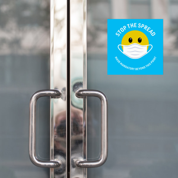Image of frosted glass doors with a square face mask sign that reads "Stop the Spread" with a smiley face wearing a mask. 