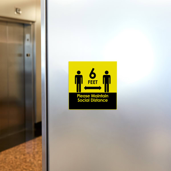 A square Avery Surface Safe sign (61513) with a bright yellow social distancing design. The sign is shown on a metal wall near elevators. 