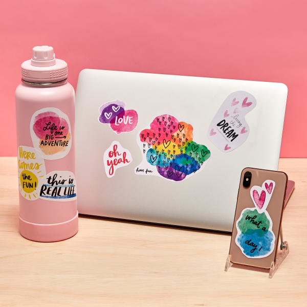 Removable decal stickers in fun rainbow colors stuck on a water bottle, laptop and smart phone.