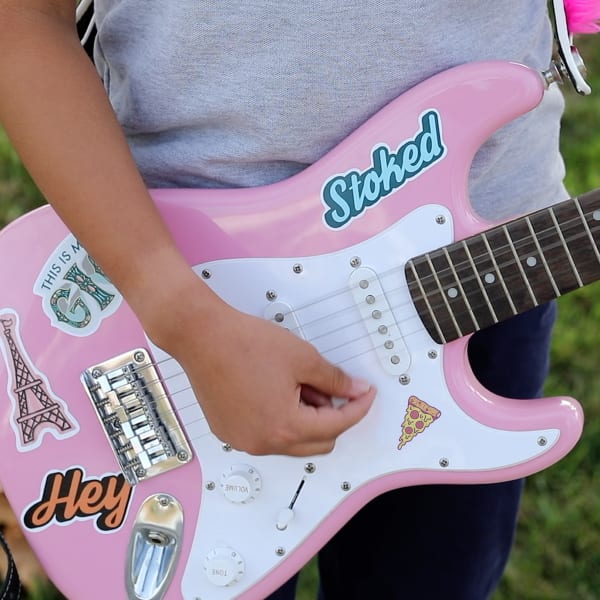 Removable decal sticker templates shown applied on a pink guitar while a kid is strumming it. 