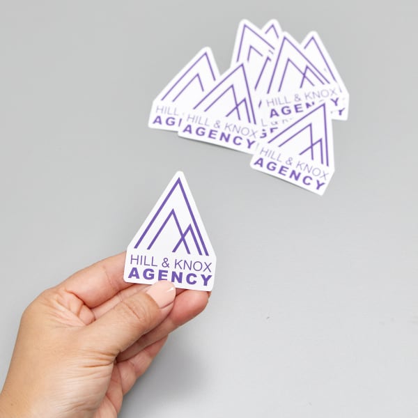 Custom printed vinyl die-cut stickers featuring a purple business logo with an interesting shape. 