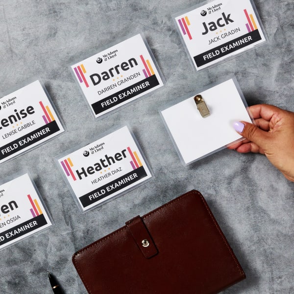 An example of a branded name tag idea for meetings the design features the company logo and colors as well as a space for names and roles. The plastic name tag holder has a clip on the back to attach to clothing. 