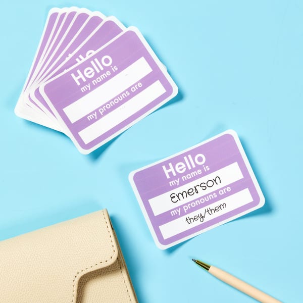 An example of "Hello My Name Is" stickers with a space for pronouns. The background is a light purple, or lavender, with white spaces to handwrite names and pronouns.