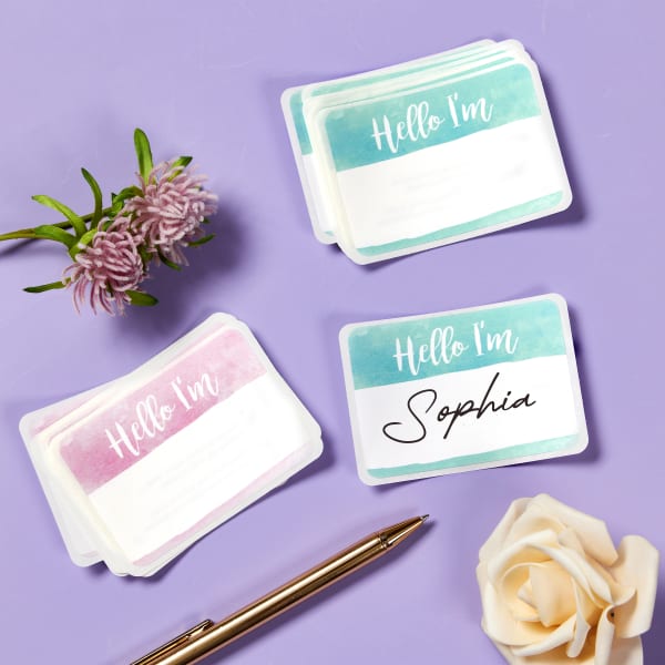 An example of pastel "Hello I'm" stickers you can print. They're shown with mint or lilac backgrounds, and read "Hello I'm" in a trendy handwritten font style. There is white space for actually handwriting individual names with a marker.