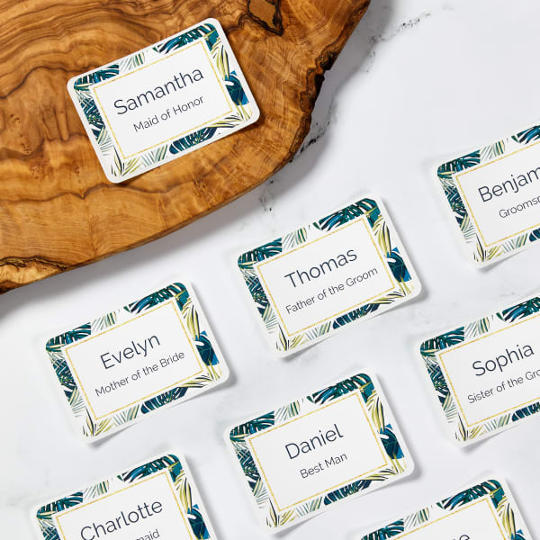 Examples of classy tropical name tags for party guests. There is a modern, fresh palm frond border with gold accents and simple sans serif font that is easy to read for names.