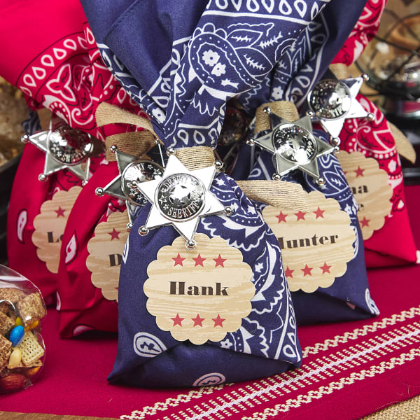 Bandanna & sheriff badge treat bag for kids party is shown personalized with Avery 8218 round labels with a scalloped edge. The design has a "wood" background and red stars to fit a western birthday party theme.