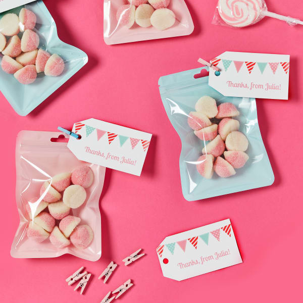 Color-coordinated candy is added to pastel bags for a personalized birthday party favor. The favors are topped off with personalized Avery 22802 tags with a pink and minty green bunting design.