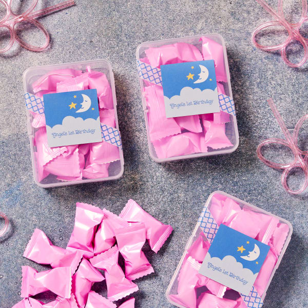 Pink candies in small containers are topped off with a personalized stars & moon-themed label. The labels are printed on Avery 22806 square labels.