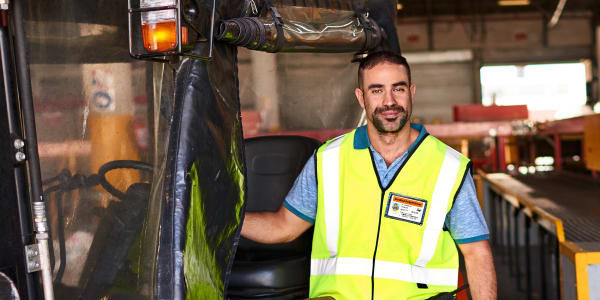 Image of warehouse worker driving a powered industrial truck forklift. Worker is wearing a certified forklift driver ID badge made with an Avery ID badge template.