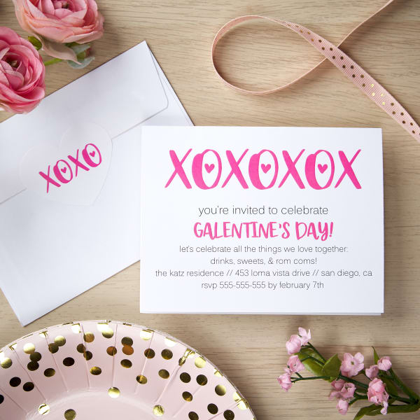 A DIY Galentine's Day party invitation shown with a matching envelope seal and pink and gold table accessories. 