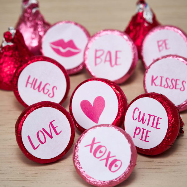 A close up of bright pink Hershey's Kisses candies showing labels on the bottom. Various cute love-themed words and graphics are printed on Avery 4221 labels. 