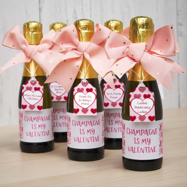 Champagne party favors for a DIY Galentine's Day party. The bottles are decorated with Avery labels and tags as well as pink and gold bows. 