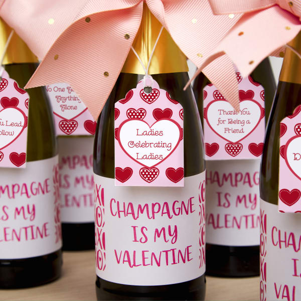 Labels that read, "Champagne is my Valentine" are printed on Avery 92407 blank labels by the sheet and applied to mini champagne bottles. Additionally Avery tags 22848 are printed with a template that features pink, red, and white hearts. The tags are personalized with Galentine's Day quotes and added to the champagne bottles.