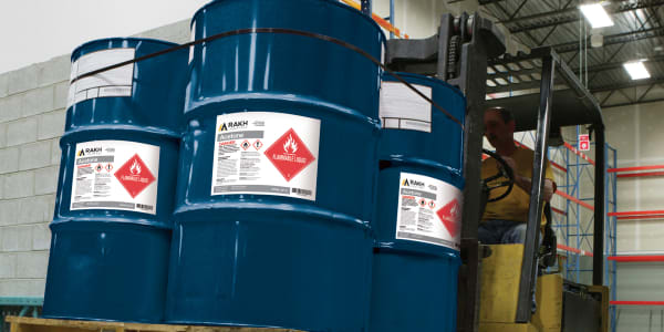 An example of primary containers for hazardous chemicals, three large drums are being transported on a forklift. Each barrel is identified with a GHS label printed on Avery 60521 UltraDuty GHS Labels.