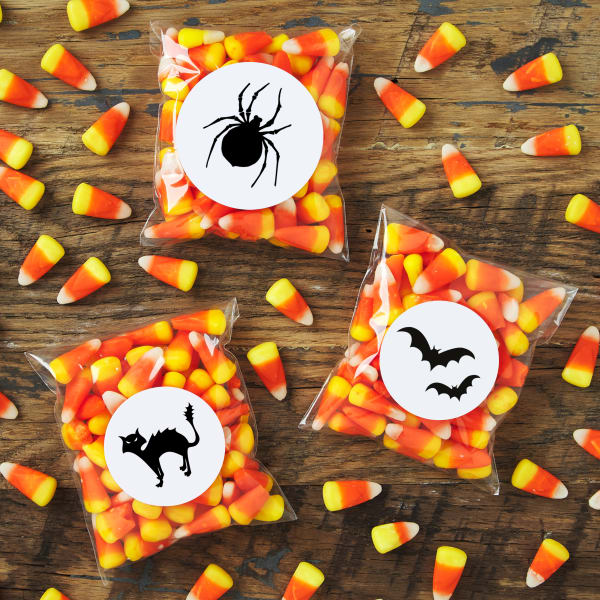DIY candy corn treats decorated with black and white Halloween labels featuring a spider, a cat and bats. 