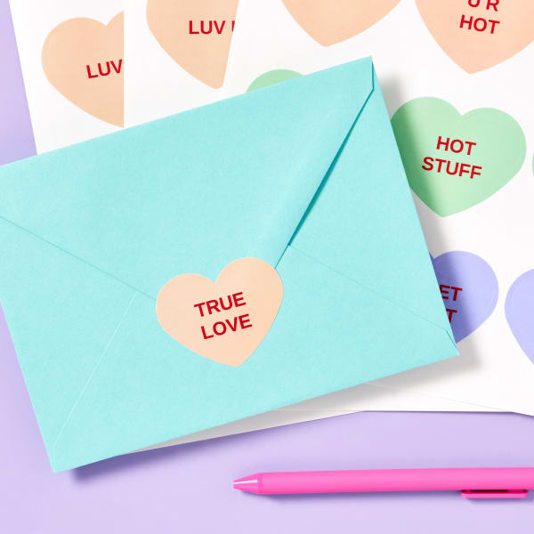 Avery 94603 heart-shaped labels printed with designs that look like the famous Valentine's candy hearts. One label is shown used as an envelope seal on a greeting card envelope. 