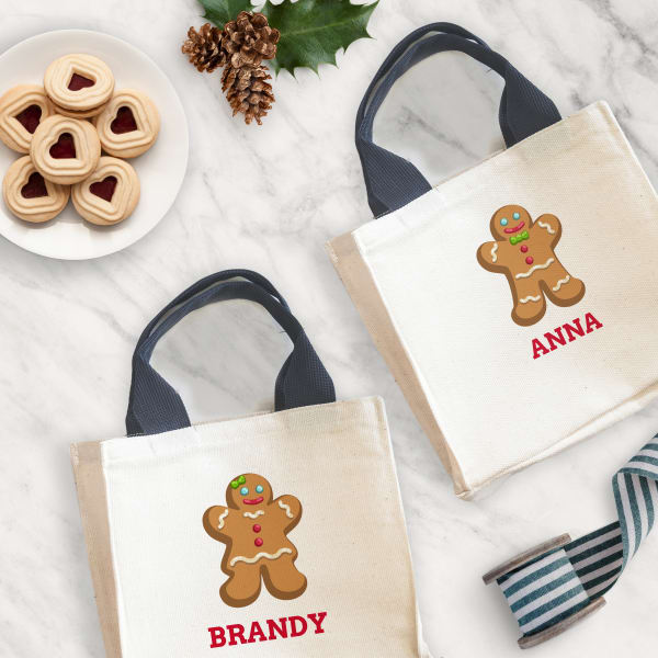 Personalized gingerbread tote bag is made with Avery fabric transfer 3271. The design on two bags feature either a gingerbread cookie person wearing pants or a gingerbread cookie person wearing a dress. Below the cookie there is cute font personalized with individual names. 