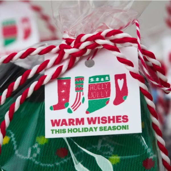 "Warm Wishes" festive stockings tag is printed on Avery square tag 22849. There are four red and green Christmas stocking graphics and the text reads, "Warm Wishes This Holiday Season!"
