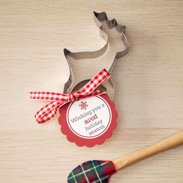 Sweet cookie cutter favors feature Avery tag 80511. The tag is printed with a red border and text that reads, "Wishing you a sweet holiday season" and is tied onto a reindeer cookie cutter. 