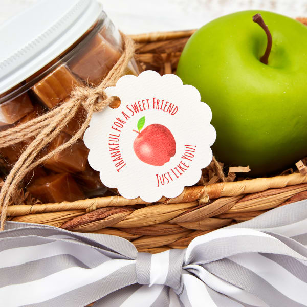 DIY caramel apple Christmas gift for coworkers features Avery scalloped tag 80511. It has a red apple graphic and reads, "Thankful for a sweet friend just like you." the tag is tied on a jar of caramel melts in a basket with a green apple. 