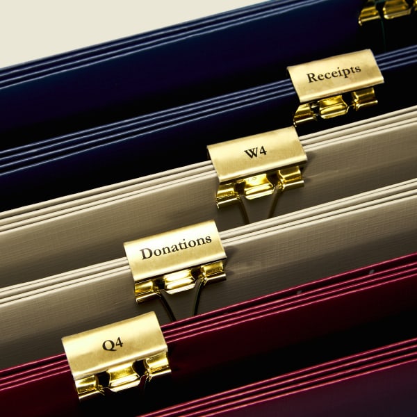 A close up of hanging file folders that have been grouped together with gold binder clips. The binder clips are labeled using clear custom-sized Avery labels so they printed on.