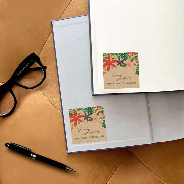 An open book with a floral bookplate design printed on a square kraft brown Avery label.