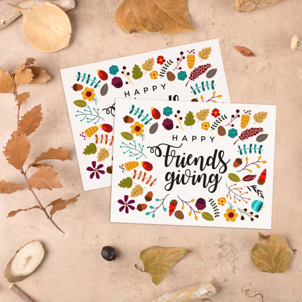 Invitations for a Friendsgiving party are shown on a tan stone background with natural leaves. 