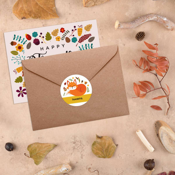 A kraft brown envelope, with a round Avery label with a cute fox design, surrounded by fall-colored leaves.